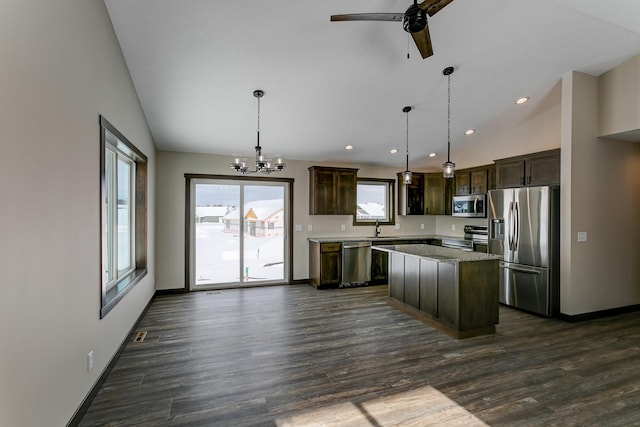 kitchen with appliances with stainless steel finishes, hanging light fixtures, vaulted ceiling, and a kitchen island