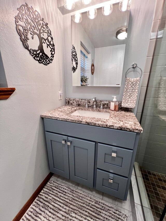 bathroom with tile patterned flooring, a tile shower, and vanity