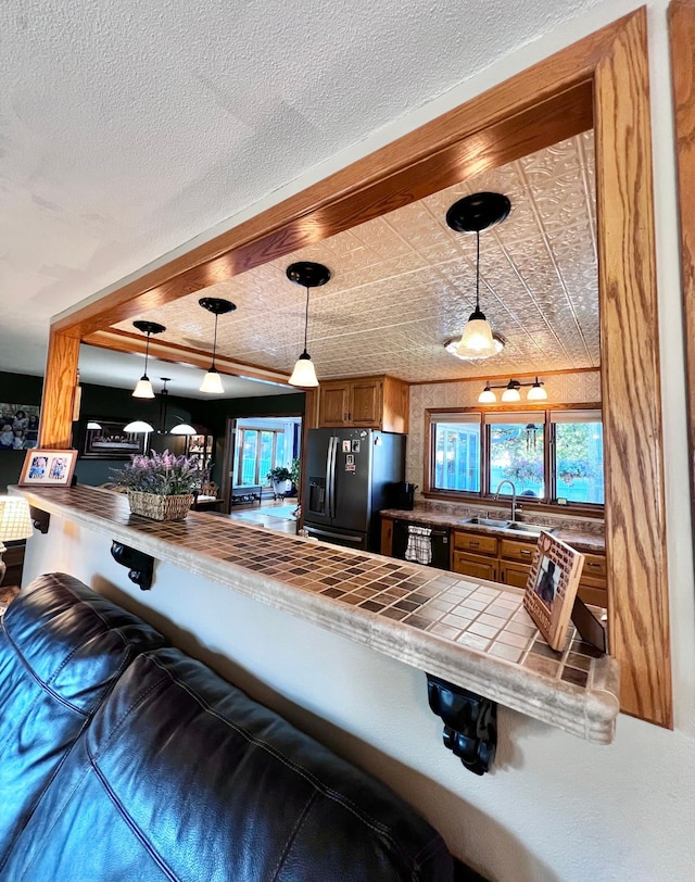 kitchen with tile counters, sink, hanging light fixtures, stainless steel fridge with ice dispenser, and kitchen peninsula