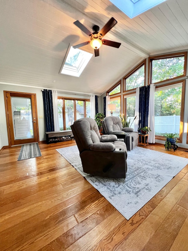 living room featuring ceiling fan, vaulted ceiling with skylight, and light wood-type flooring