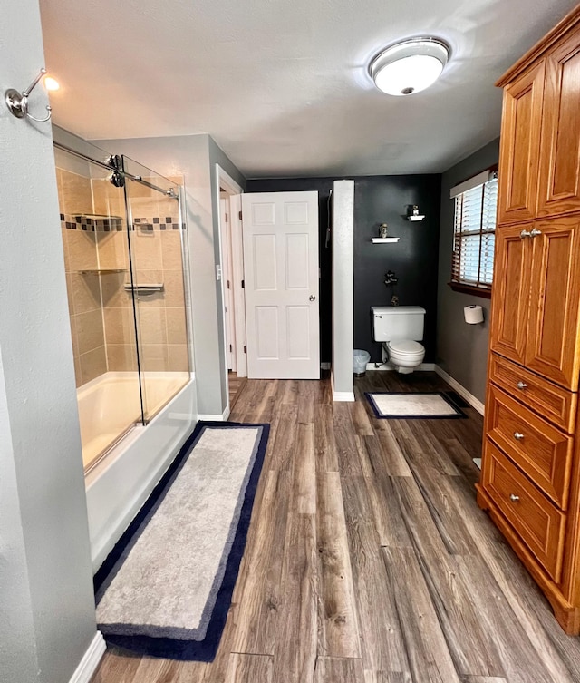 bathroom featuring hardwood / wood-style floors, enclosed tub / shower combo, and toilet