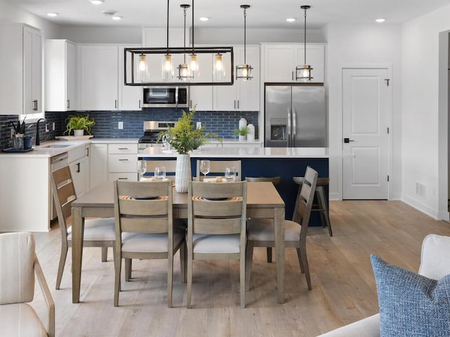 kitchen featuring light hardwood / wood-style flooring, hanging light fixtures, sink, white cabinetry, and appliances with stainless steel finishes