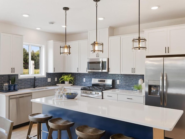 kitchen with appliances with stainless steel finishes, white cabinets, a kitchen island, and pendant lighting