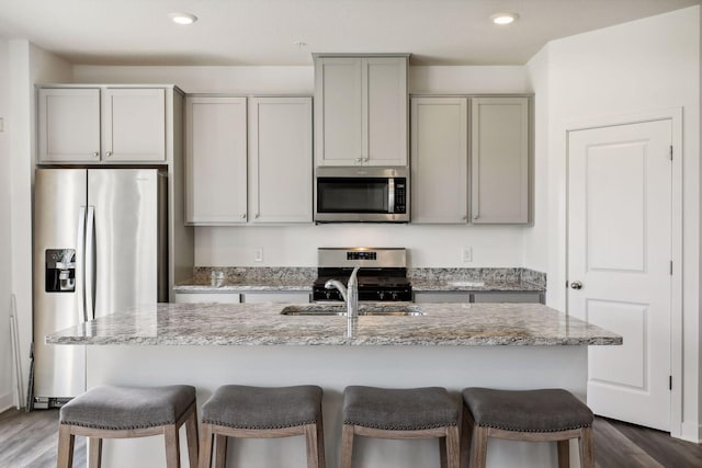 kitchen with light stone countertops, appliances with stainless steel finishes, gray cabinets, and a center island with sink