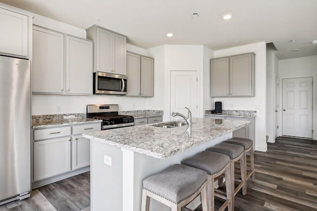 kitchen with stainless steel appliances, sink, a kitchen island with sink, and dark hardwood / wood-style flooring