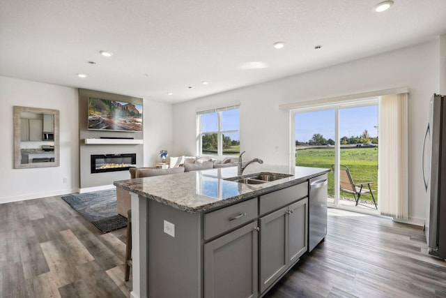 kitchen featuring sink, light stone counters, a center island with sink, appliances with stainless steel finishes, and gray cabinets