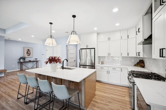 kitchen featuring appliances with stainless steel finishes, light wood-type flooring, a kitchen island with sink, sink, and hanging light fixtures