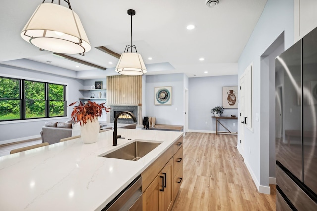 kitchen featuring sink, stainless steel appliances, light stone counters, light hardwood / wood-style floors, and a fireplace