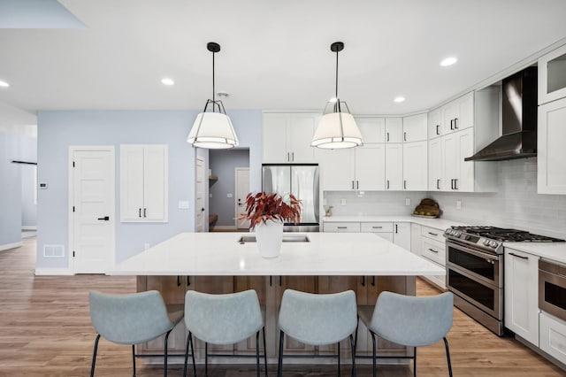 kitchen featuring backsplash, a kitchen breakfast bar, stainless steel appliances, and wall chimney exhaust hood