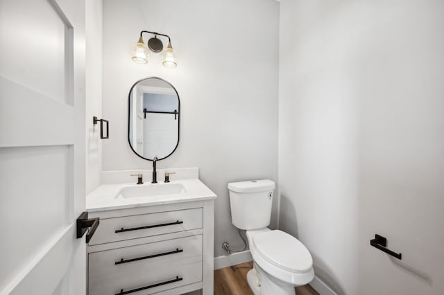 half bathroom featuring toilet, vanity, baseboards, and wood finished floors