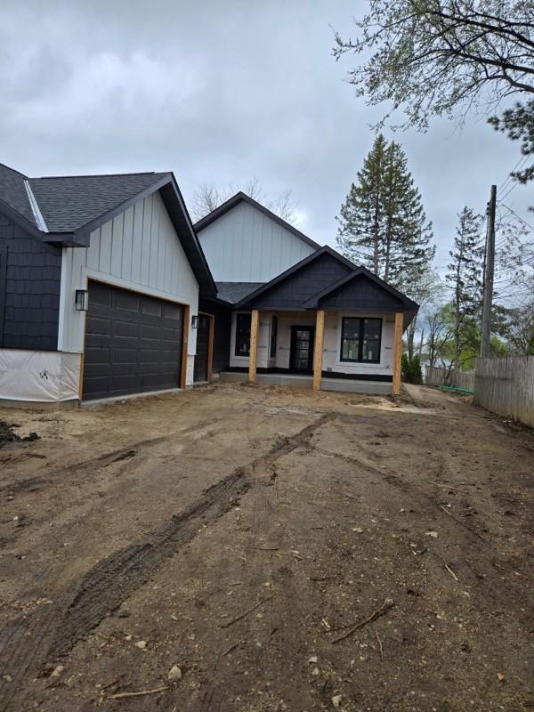 view of front of property featuring a garage, fence, a shingled roof, board and batten siding, and driveway