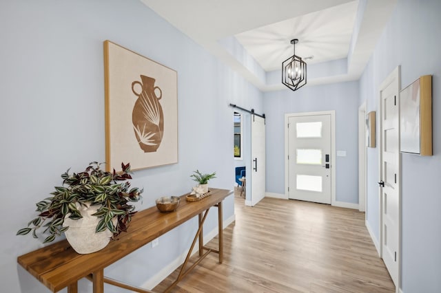 foyer featuring light wood-type flooring, baseboards, an inviting chandelier, and a barn door