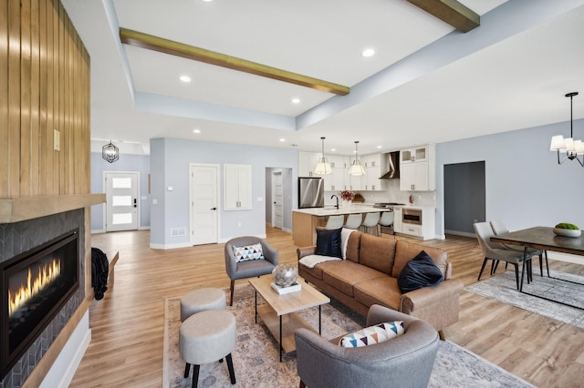 living room with beam ceiling, light wood-type flooring, a fireplace, an inviting chandelier, and baseboards