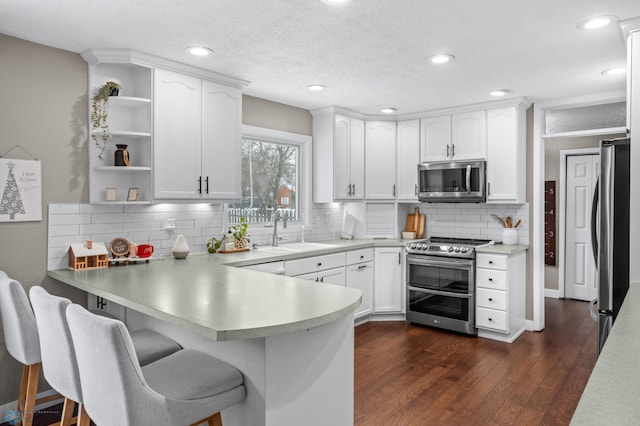 kitchen with kitchen peninsula, appliances with stainless steel finishes, sink, white cabinets, and dark hardwood / wood-style floors