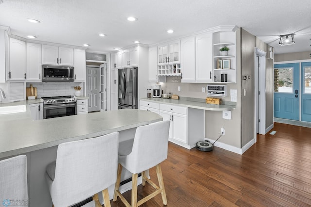 kitchen featuring white cabinetry, stainless steel appliances, dark hardwood / wood-style flooring, kitchen peninsula, and a breakfast bar