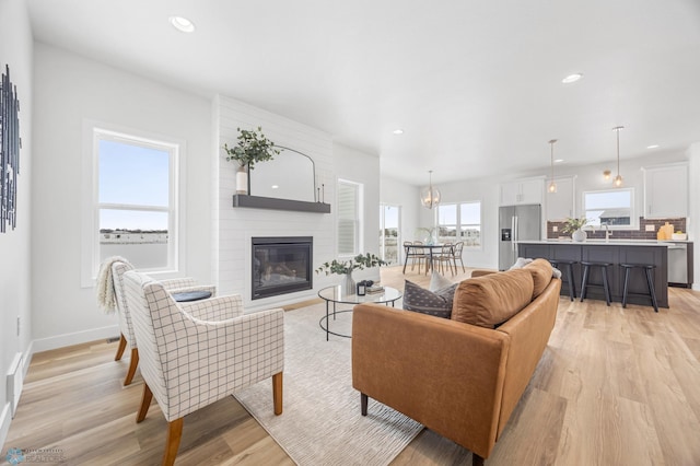 living area featuring a large fireplace, baseboards, light wood finished floors, and recessed lighting