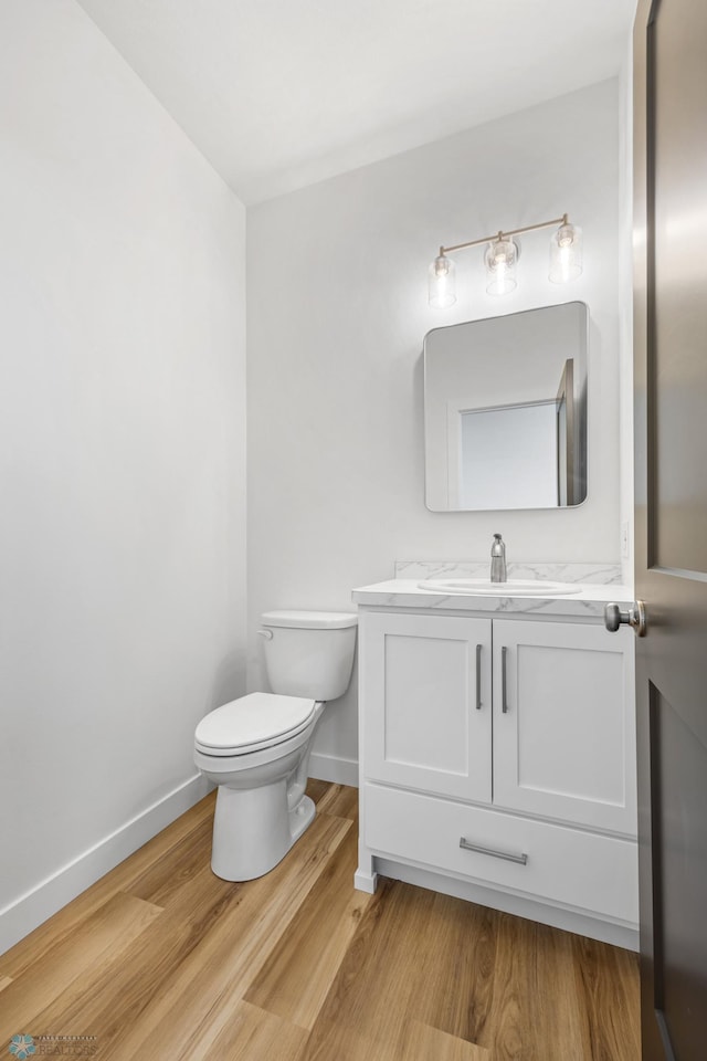 half bath featuring toilet, vanity, baseboards, and wood finished floors