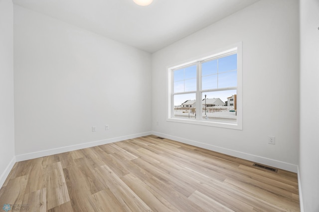 empty room featuring baseboards, light wood finished floors, and visible vents