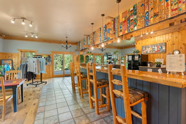 bar with ornamental molding, decorative light fixtures, wood walls, and black refrigerator with ice dispenser