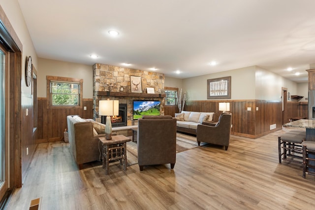 living room featuring wood walls, a stone fireplace, and light hardwood / wood-style floors