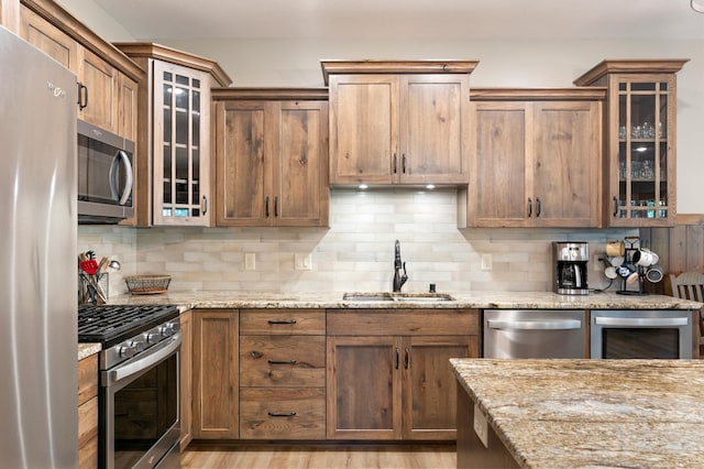 kitchen with light wood-type flooring, light stone counters, stainless steel appliances, sink, and wine cooler