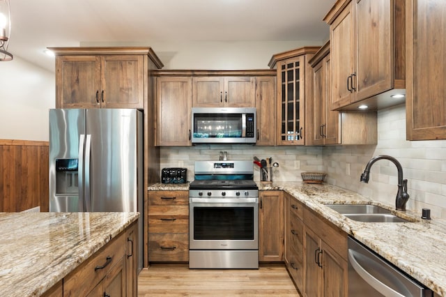 kitchen with backsplash, stainless steel appliances, sink, light stone countertops, and light hardwood / wood-style floors