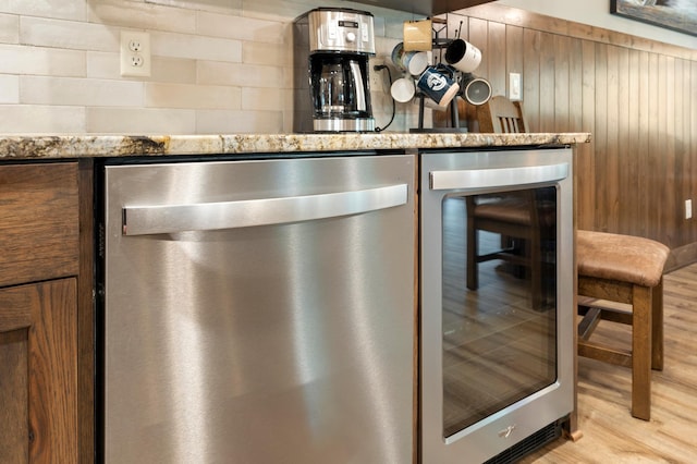 interior details featuring wood walls, beverage cooler, light hardwood / wood-style floors, stainless steel dishwasher, and bar area