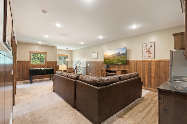 living room with an inviting chandelier, light carpet, and wooden walls