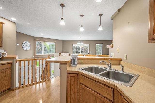 kitchen featuring hanging light fixtures, sink, a textured ceiling, an inviting chandelier, and light hardwood / wood-style floors