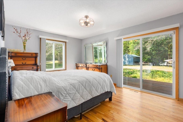 bedroom featuring multiple windows, access to exterior, light hardwood / wood-style floors, and a textured ceiling