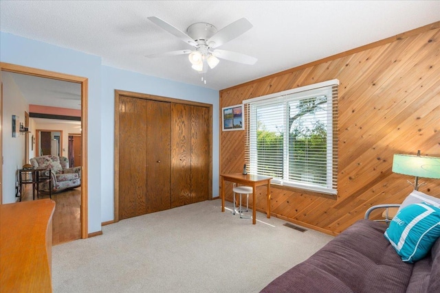 sitting room with ceiling fan, wooden walls, and light carpet