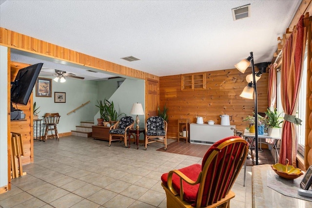 living room with ceiling fan, wooden walls, and a textured ceiling