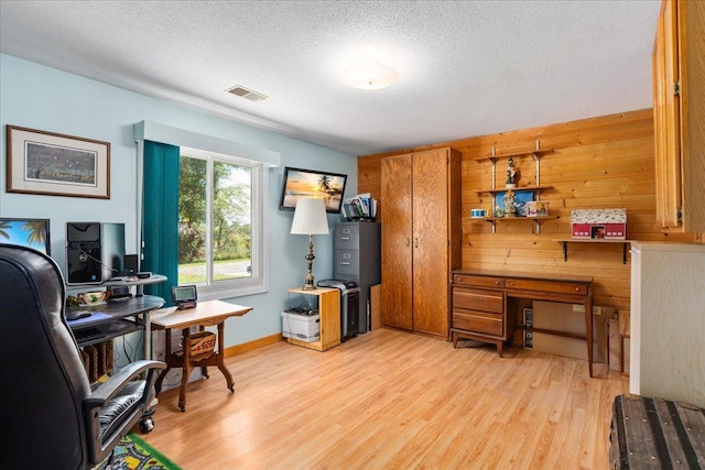 office space featuring wooden walls, light hardwood / wood-style floors, and a textured ceiling