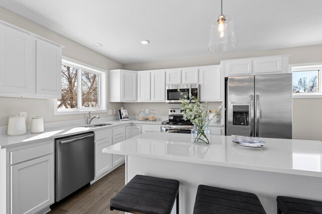 kitchen with a kitchen bar, dark wood-type flooring, stainless steel appliances, sink, and white cabinetry