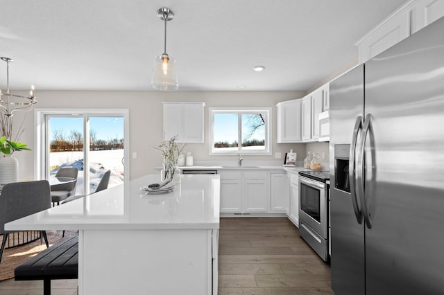 kitchen featuring hanging light fixtures, hardwood / wood-style floors, appliances with stainless steel finishes, white cabinetry, and sink