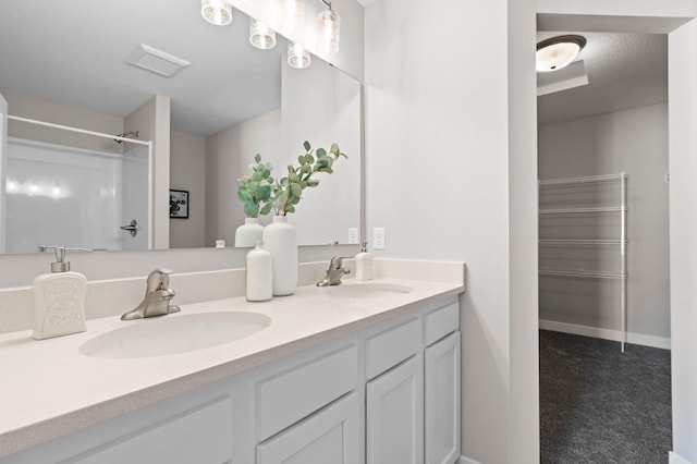 bathroom with a textured ceiling, vanity, and a shower