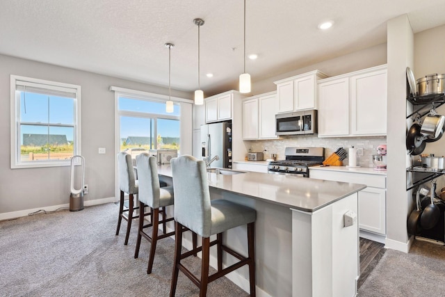 kitchen with appliances with stainless steel finishes, sink, a center island with sink, white cabinetry, and hanging light fixtures