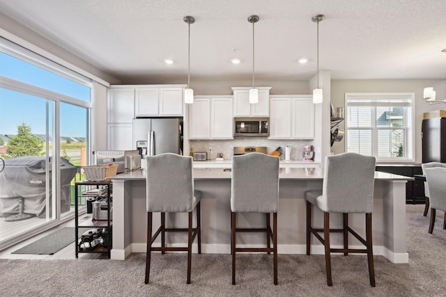 kitchen featuring a kitchen breakfast bar, white cabinetry, hanging light fixtures, and appliances with stainless steel finishes