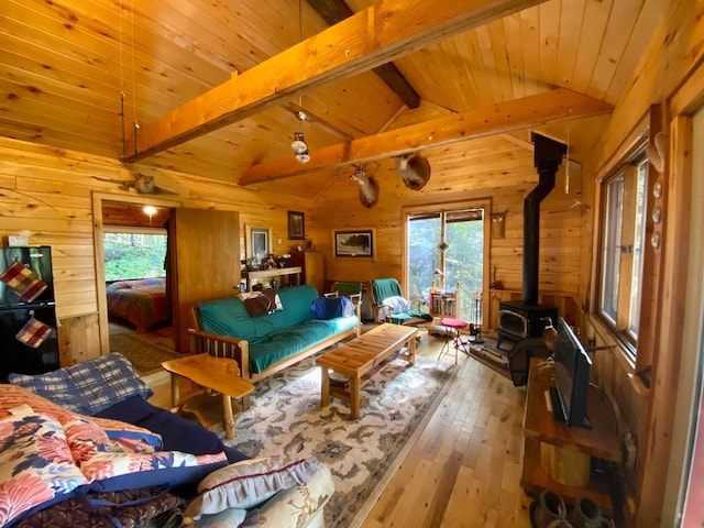 living room featuring hardwood / wood-style flooring, plenty of natural light, a wood stove, and vaulted ceiling with beams