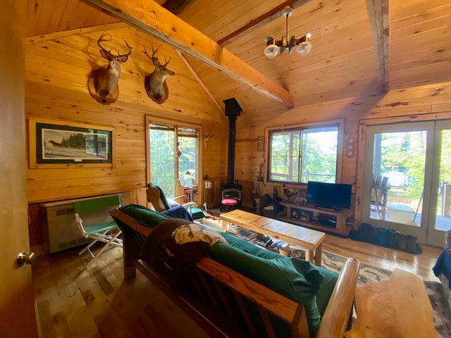 living room featuring wood walls, wooden ceiling, a wood stove, wood-type flooring, and beam ceiling