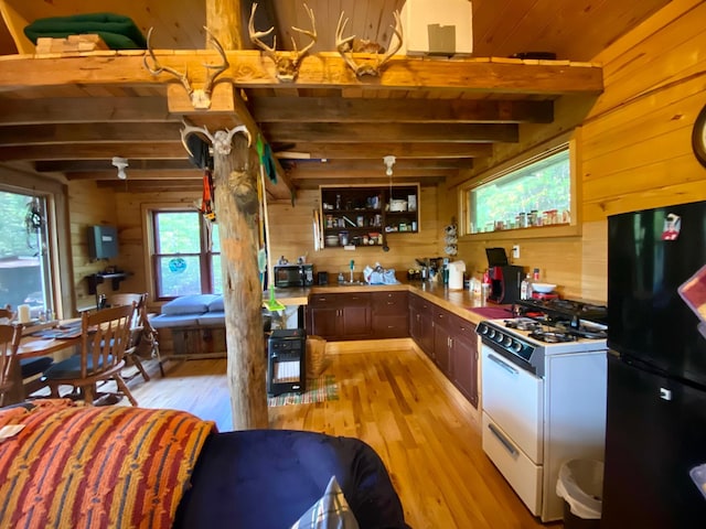 kitchen with beamed ceiling, black appliances, a wealth of natural light, and wood walls