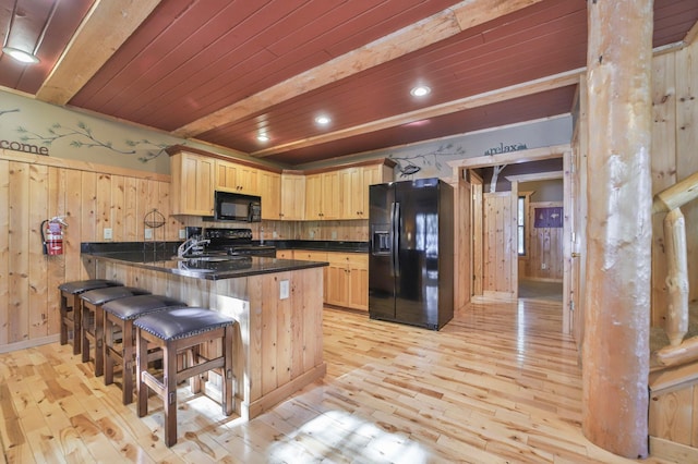 kitchen featuring light wood-type flooring, wooden walls, black appliances, light brown cabinetry, and kitchen peninsula