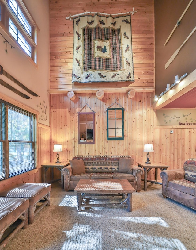 living room featuring a wealth of natural light, a high ceiling, wooden walls, and carpet floors