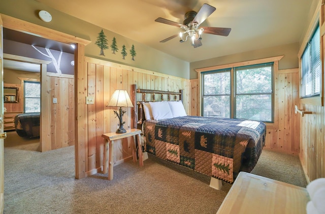 bedroom featuring multiple windows, ceiling fan, carpet, and wood walls