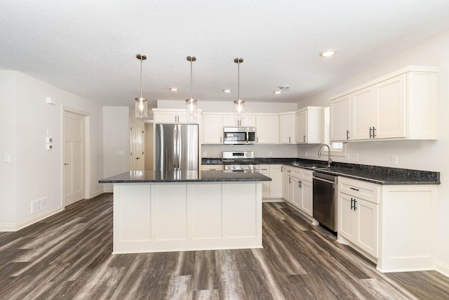 kitchen featuring a kitchen island, dark hardwood / wood-style floors, hanging light fixtures, white cabinets, and appliances with stainless steel finishes