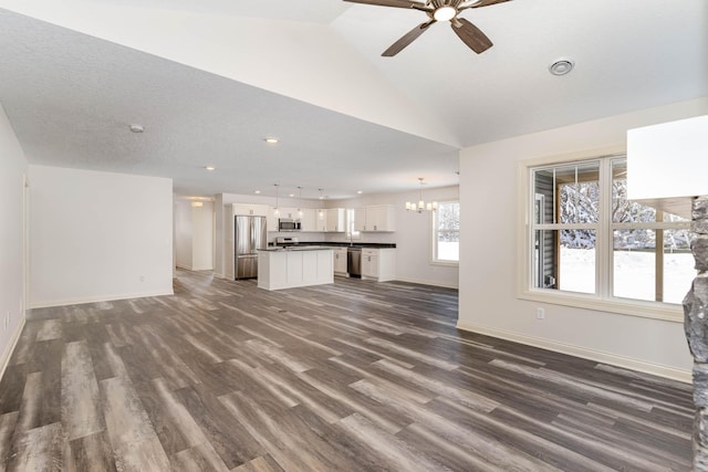 unfurnished living room featuring ceiling fan with notable chandelier, a textured ceiling, lofted ceiling, and dark hardwood / wood-style floors