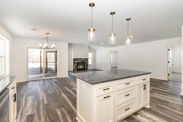 kitchen with stainless steel dishwasher, dark hardwood / wood-style floors, white cabinets, dark stone counters, and hanging light fixtures