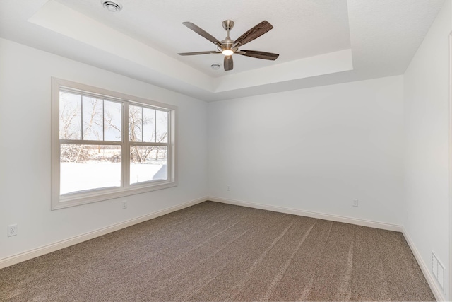 carpeted spare room featuring ceiling fan and a raised ceiling