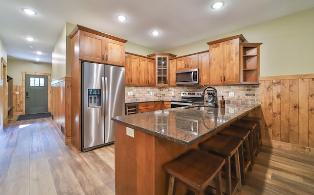 kitchen featuring dark stone countertops, light hardwood / wood-style flooring, kitchen peninsula, a breakfast bar, and appliances with stainless steel finishes