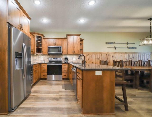 kitchen featuring a breakfast bar area, decorative light fixtures, stainless steel appliances, sink, and light wood-type flooring